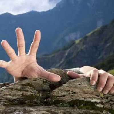 Two hands reaching up over cliff edge wth one hand outstretched in need of help
